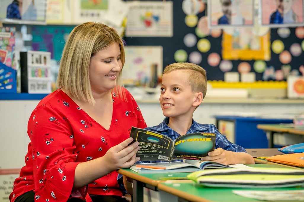 Teacher sitting with student and reading a book. 
